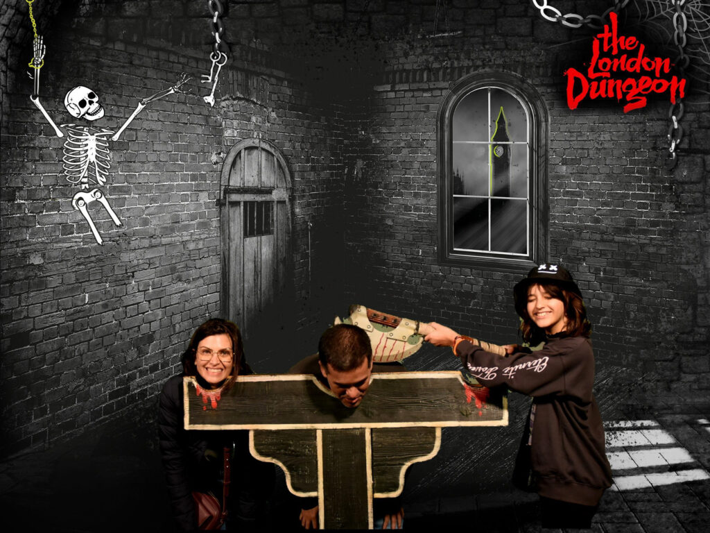 foto com efeito especial da atração london dungeon, duas pessoas com a cabeça em um cadafalso e outra fingindo ser o carrasco