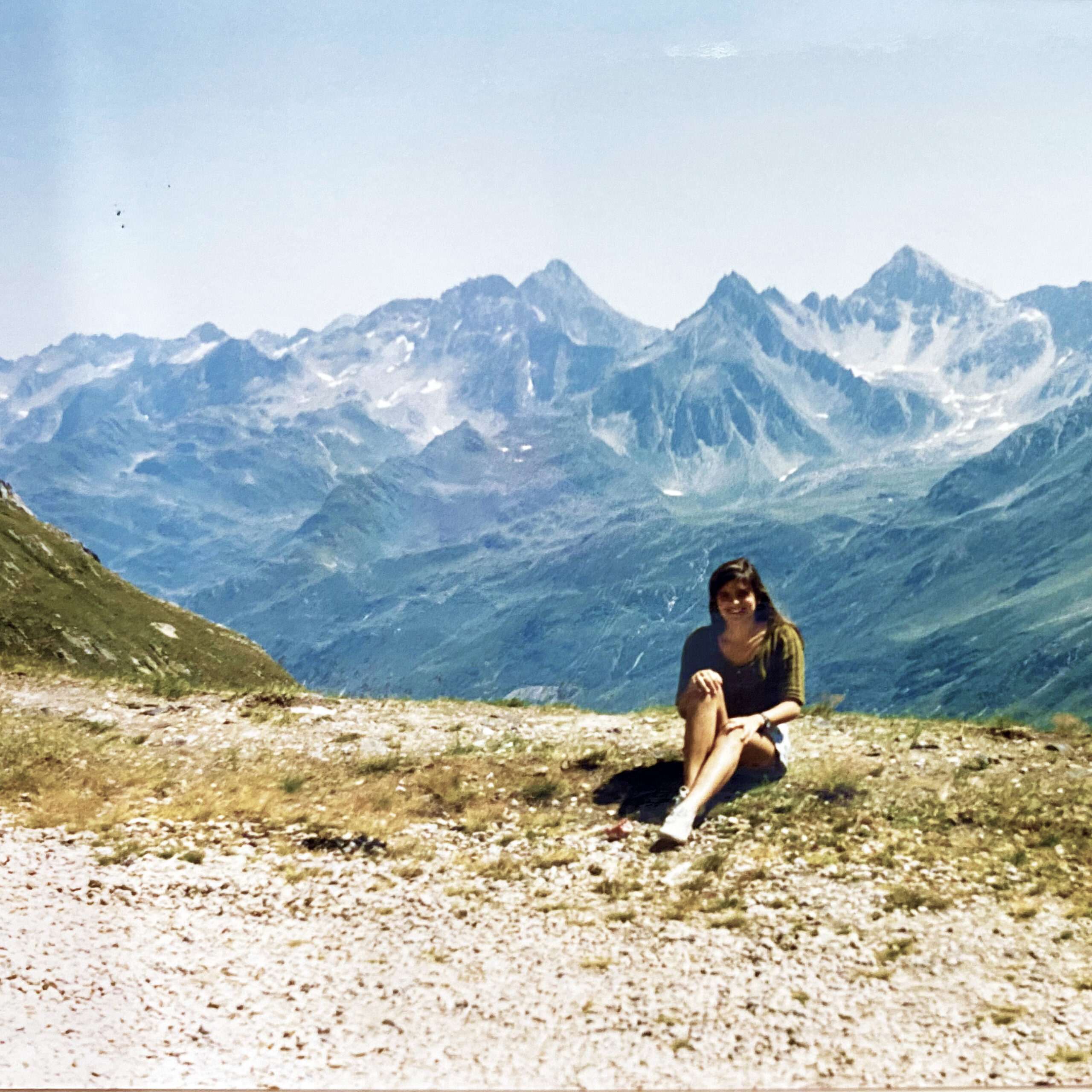 jovem sentada em um gramado com os alpes austríacos ao fundo nos anos 90.