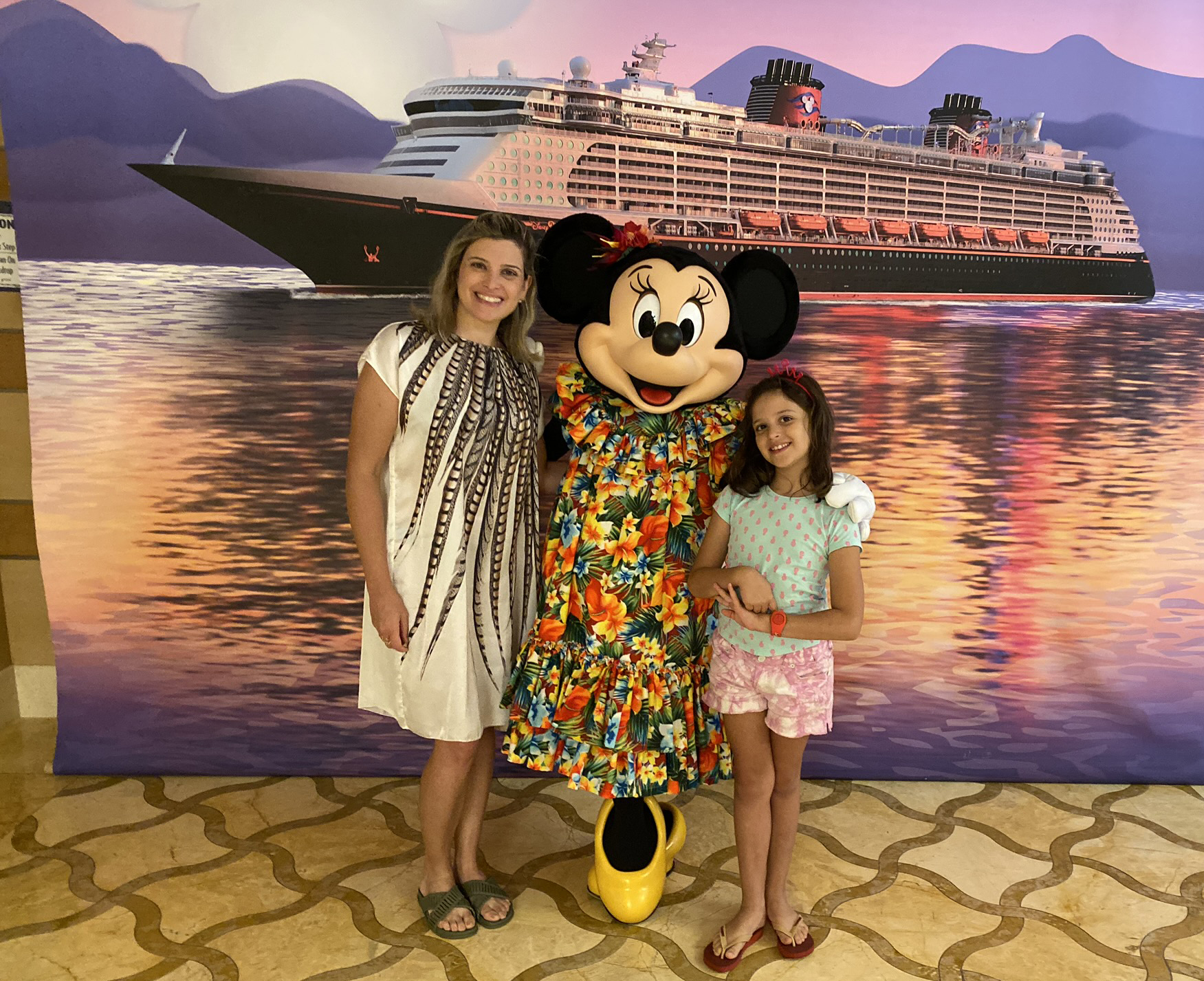 mãe e filha tirando foto com a Minnie de figurino caribenho com banner do navio da Disney Crius Line ao fundo