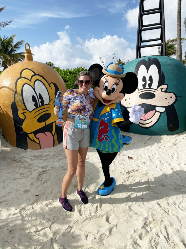 mulher corredora ganhando uma medalha na corrdia de 5Km do cruzeiro da Disney, posando com a Minnie com figurino de resort