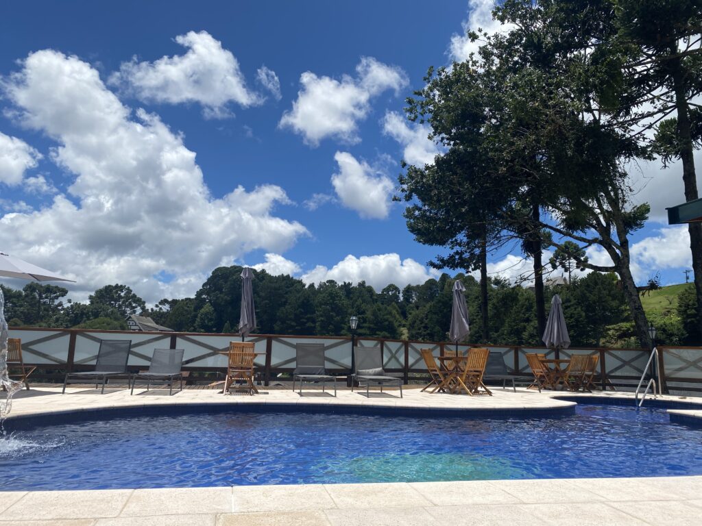 piscina de hotel cm ceu azul, nuvens, arvores e espreguiçadeiras