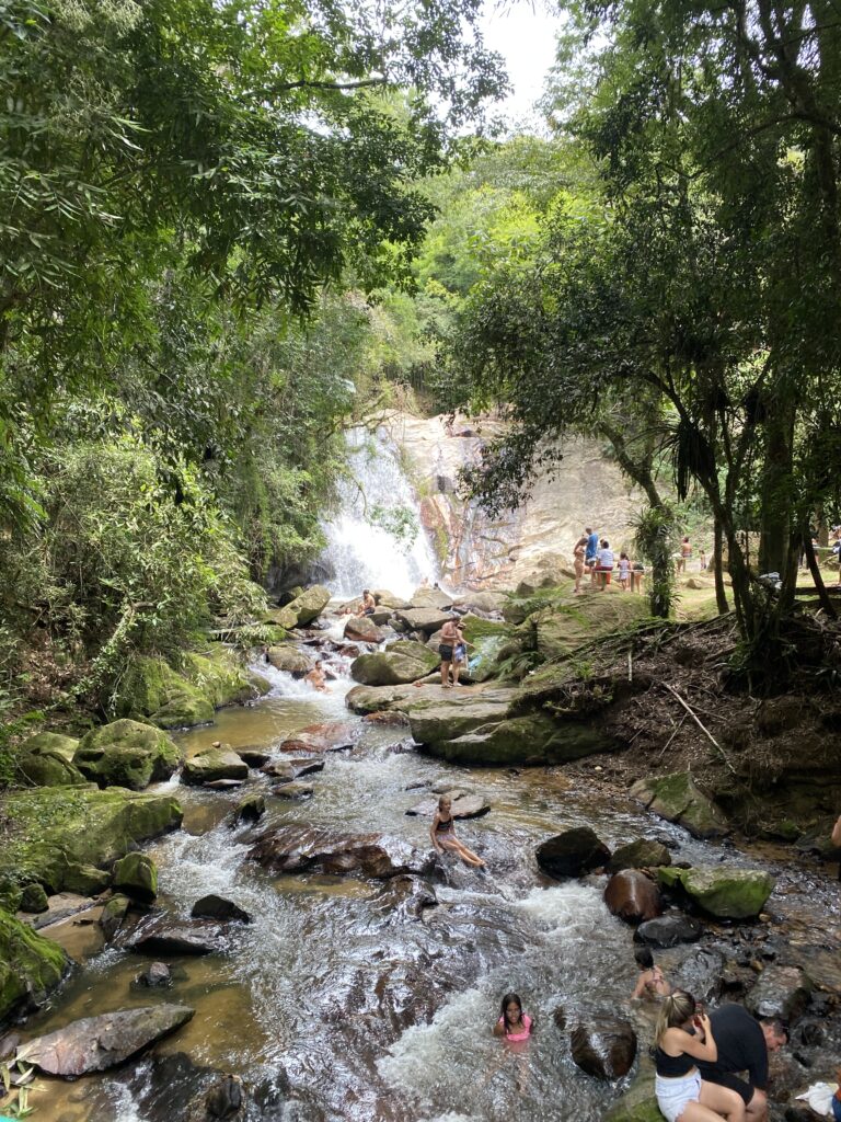 cachoeira cercada de verde com poço para banho onde há pessoas nadando