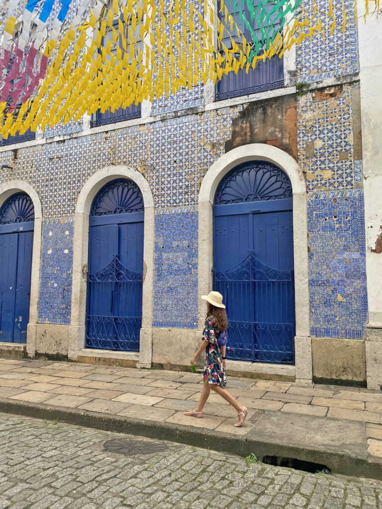 Criança passeando na Rua Potugal em São Luis do Maranhão, com casarão de fachada de azulejos azuis ao fundo e bandeirinhas de São João penduradas na rua