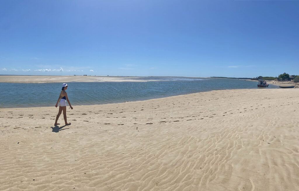 menina passeando na praia com banco de areia e psicina de água do mar