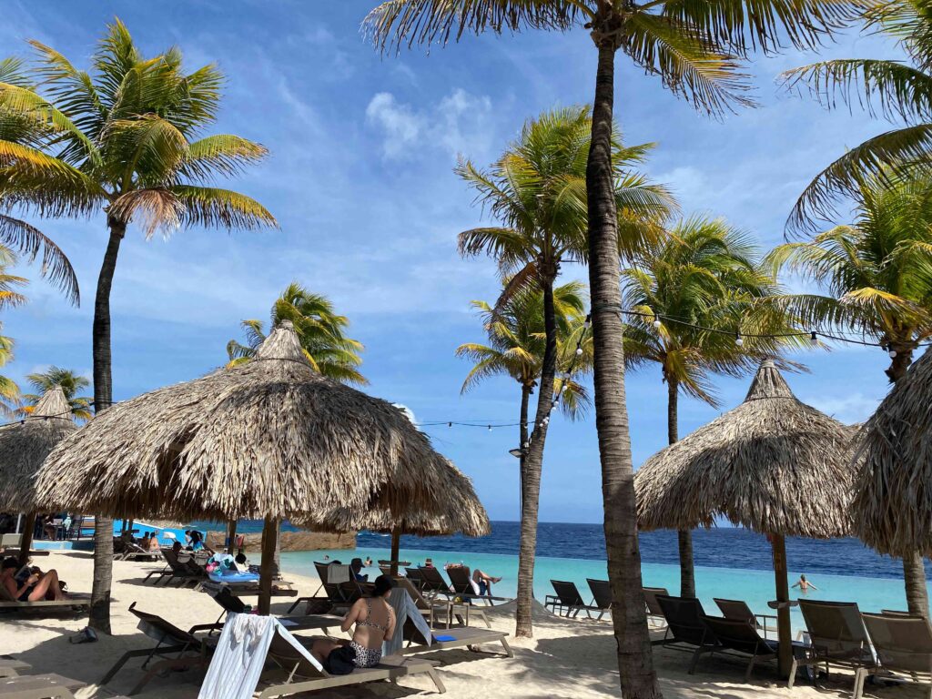 imagem da praia/piscina do hotel renaissance em curaçao com espreguiçadeiras, palapas e coqueiros