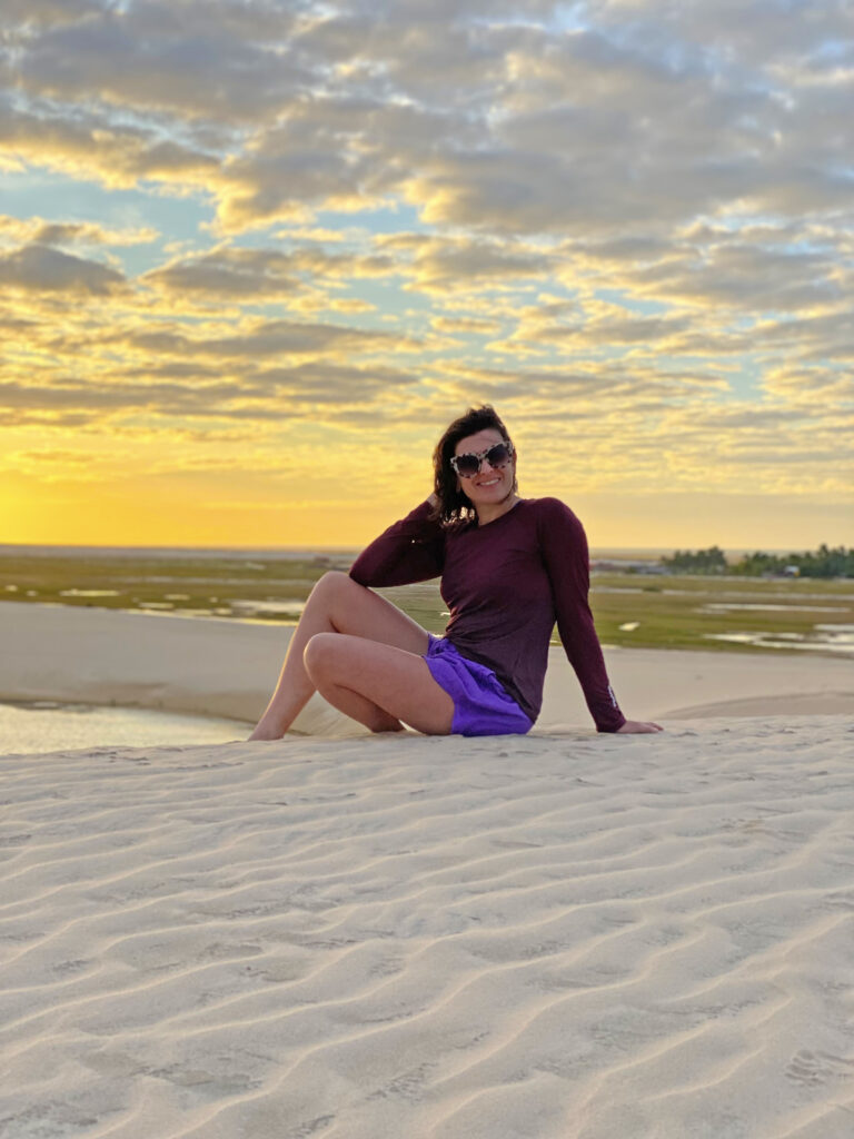 mulher sentada em uma duna de areia branca vendo o por do sol