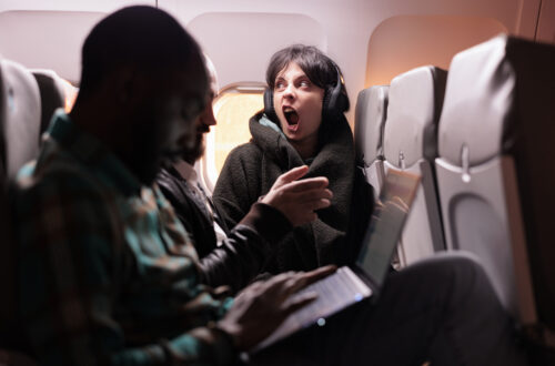 Multiethnic group of people flying abroad in economy class, using laptop, smartphone and headphones during sunset flight. Passengers travelling with international commercial airline.