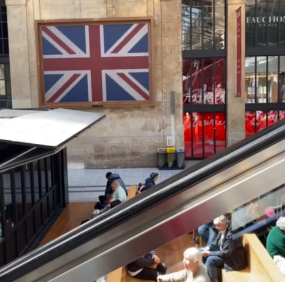 estação gare du nord com escadas rolantes que levam ao embarque do eurostar e a bandeira do reinoa unido ao fundo