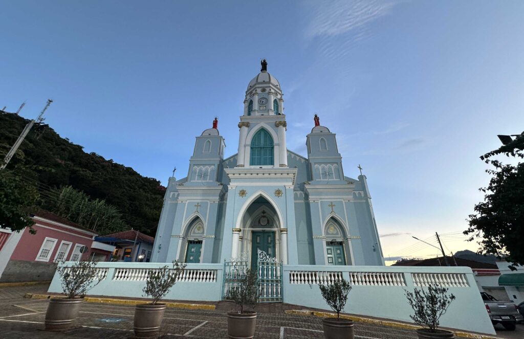 A fachada azul clara da igreja matriz de São Bento do Sapucai com o por do sol atras.