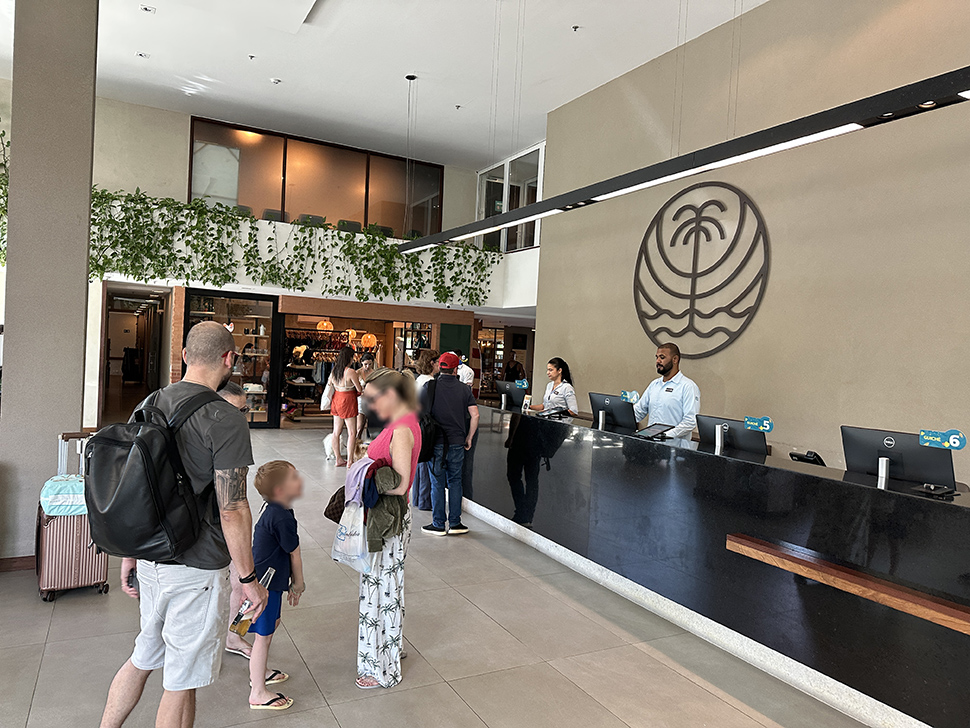 recepção do resort Japaratinga, com balcão preto, 2 recepcionistas e vários hóspedes fazendo check in