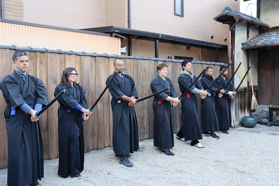 Turistas vestidos de samurai treinando com espada de madeira no dojo
