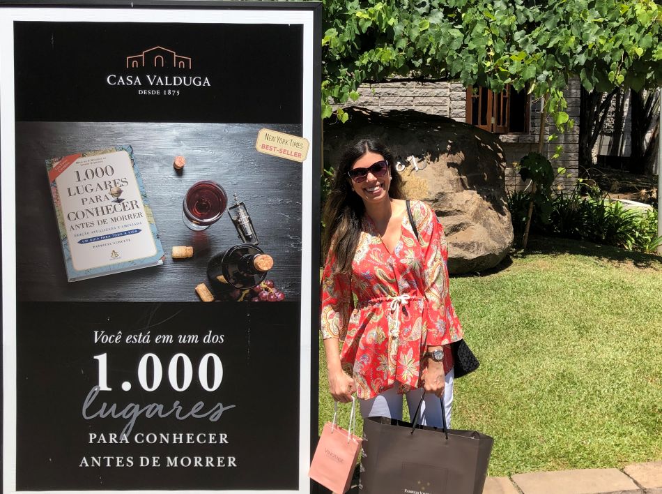 cartaz com o nome da vinicola Casa Valduga e mulher com sacola de vinhos que comprou na loja